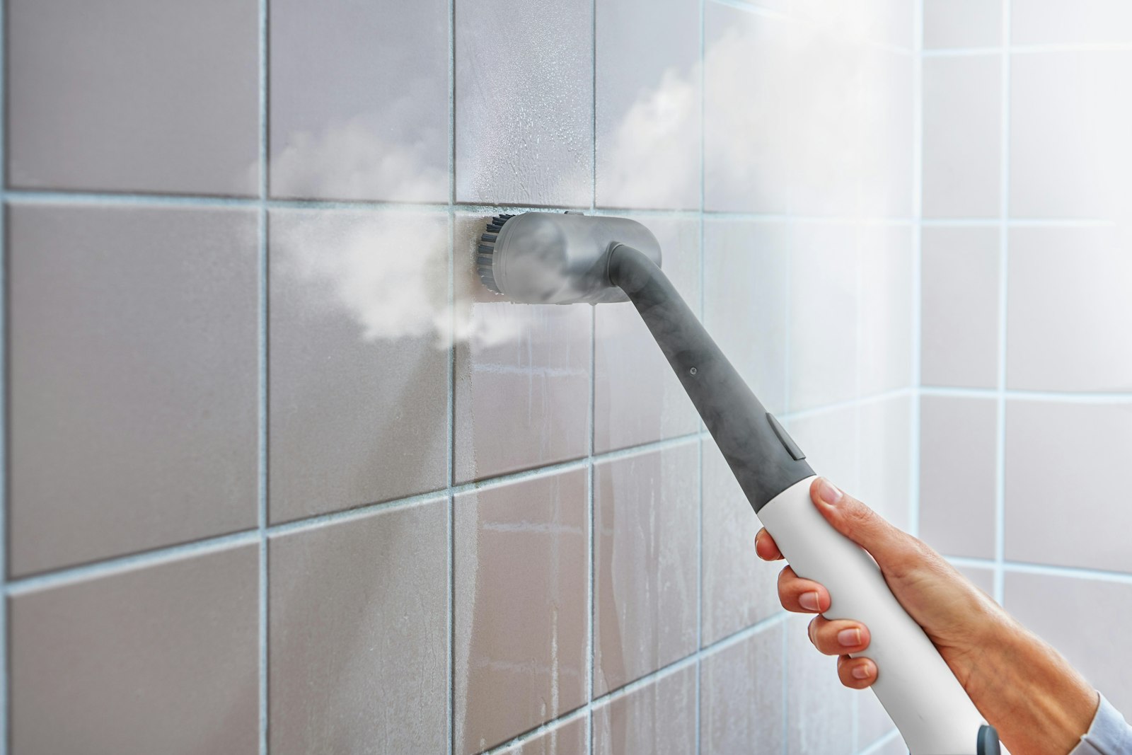 Steam cleaner sanitising a tiled bathroom wall