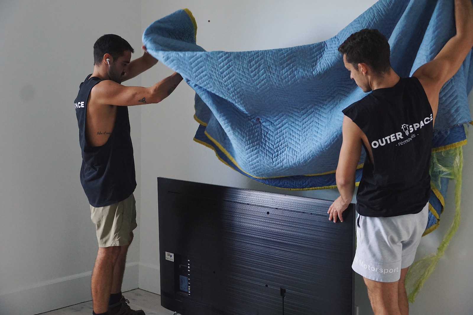 Two Outer Space movers wrapping a TV in a moving blanket