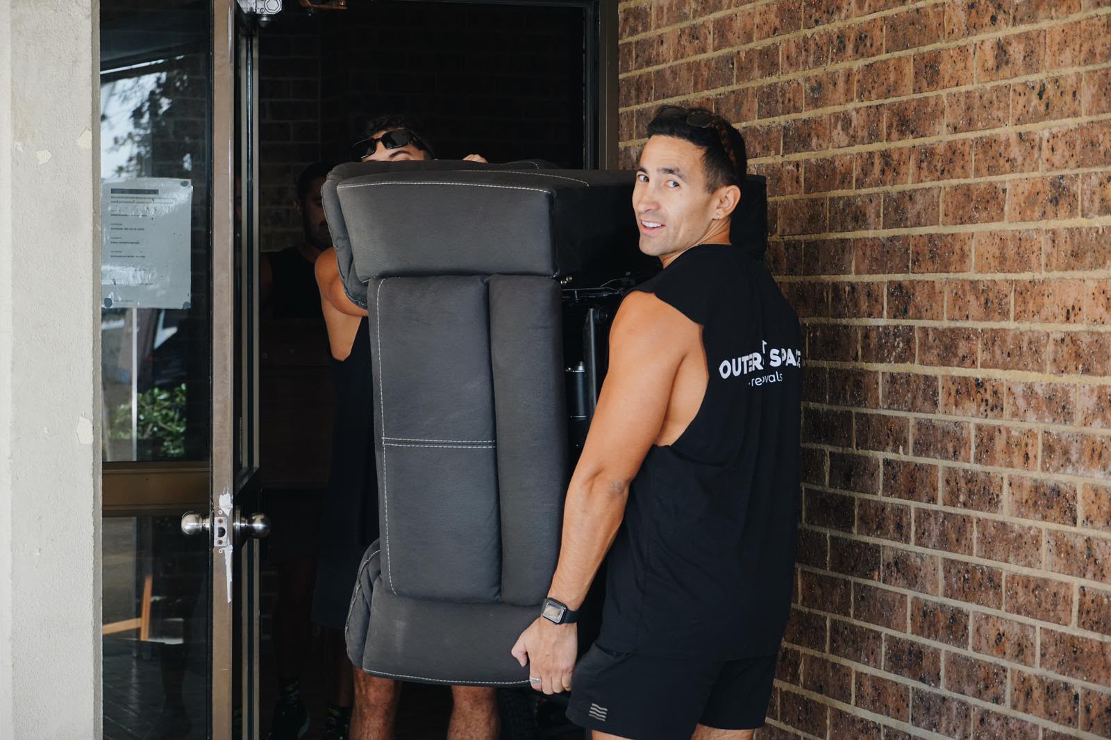 Felix, co-founder of Outer Space Removals, carrying a recliner sofa into a Sydney apartment